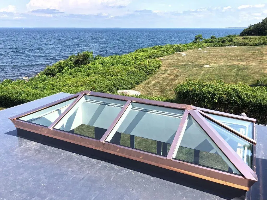 Glass skylight on a rooftop overlooking the ocean and grassy coastline.