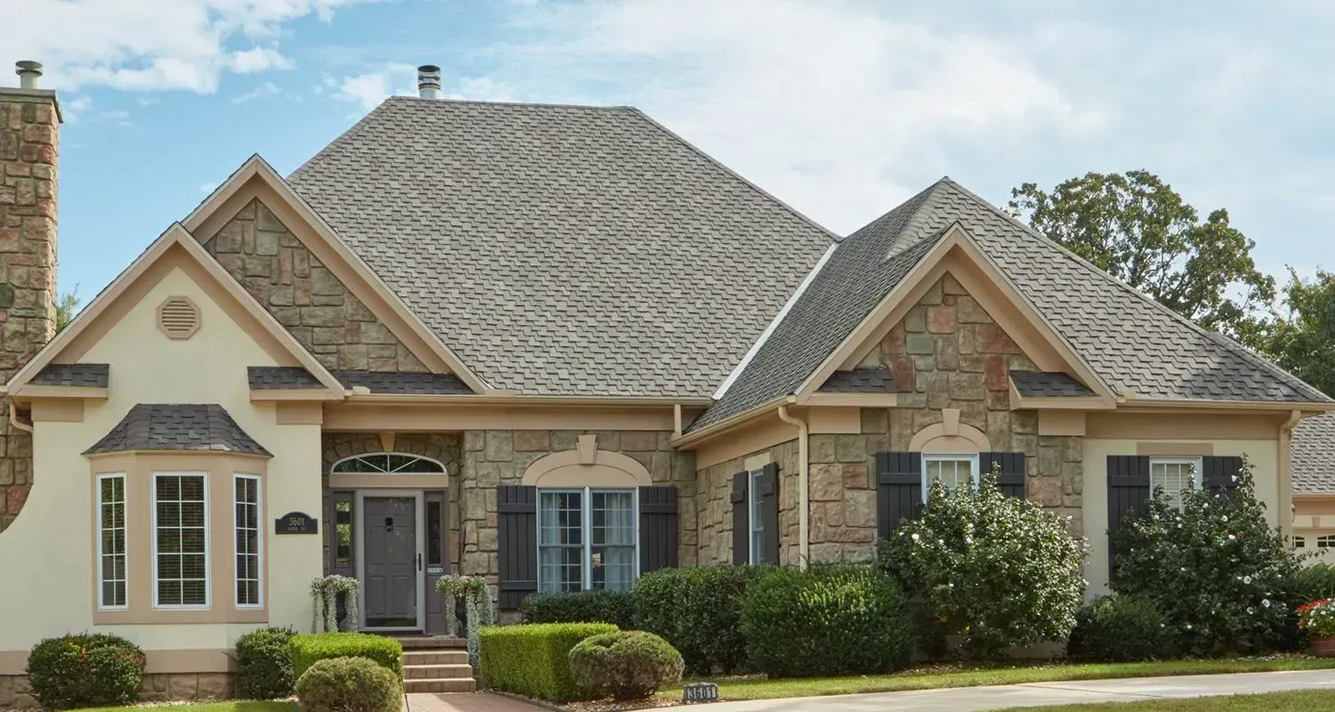Suburban house with stone and brick exterior, gray roof, and landscaped front yard under a blue sky