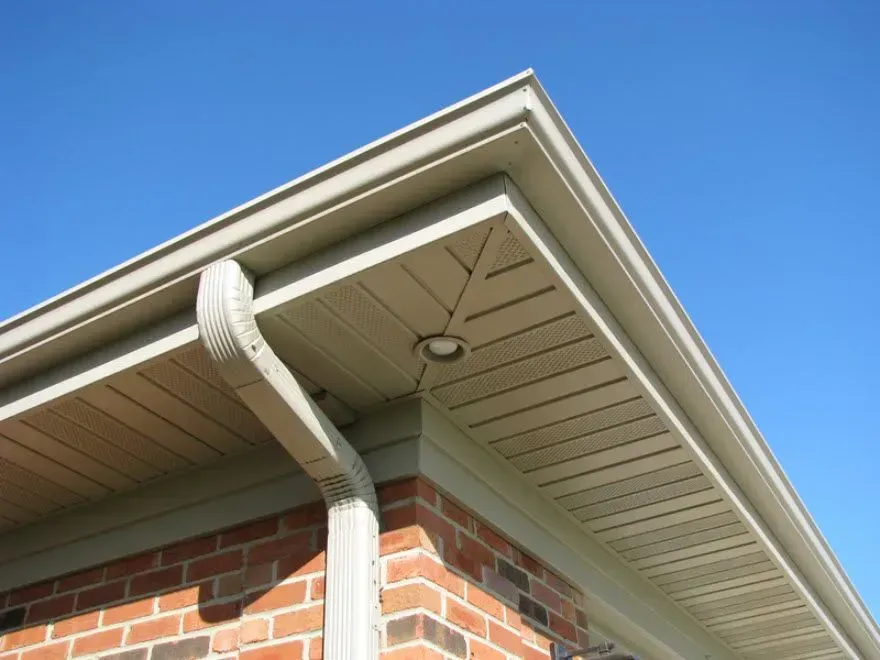 Corner of a brick house with white gutter and beige soffit against a blue sky