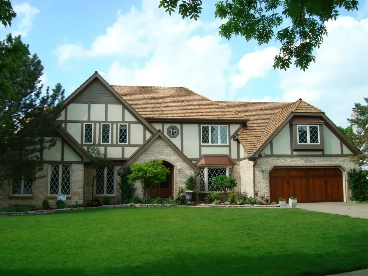 Large Tudor-style suburban house with a red garage, green lawn, and trees framing the front yard