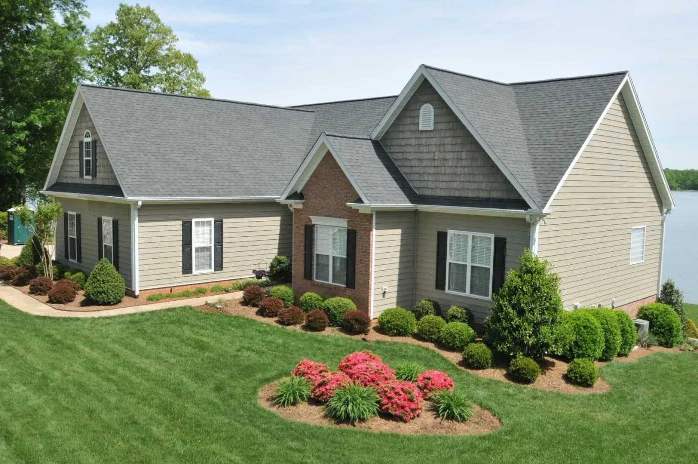 Suburban house with gray roof, beige siding, manicured lawn, and landscaped flower beds