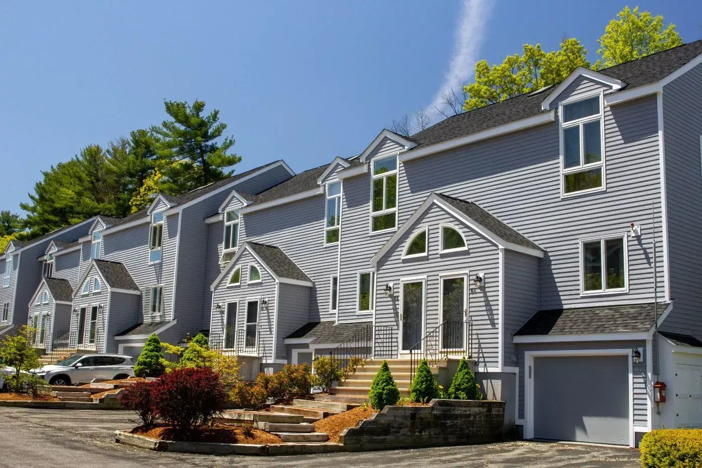 Row of gray townhouses with white trim and garages, landscaped front yard, under a clear blue sky