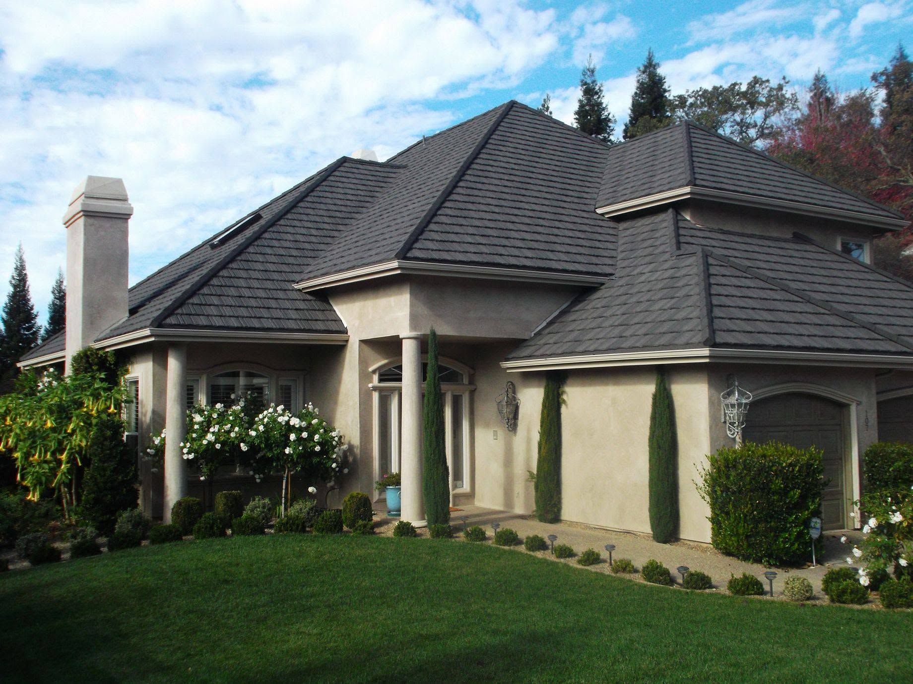 Suburban house with a dark shingled roof, beige stucco walls, and a green lawn under a blue sky