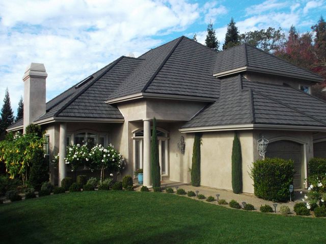 Suburban house with gray shingled roof, chimney, and manicured green lawn under a blue sky