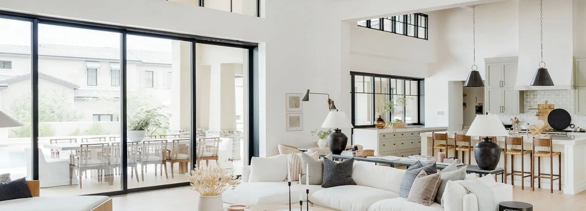 Bright modern open-plan living room and kitchen with large windows, white decor, and a seated person on a sofa