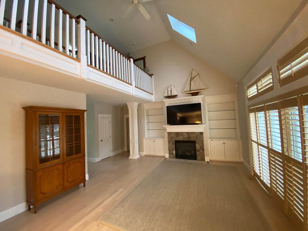 Bright open living room with vaulted ceiling, loft railing, fireplace, built-in cabinets, and wood shutters