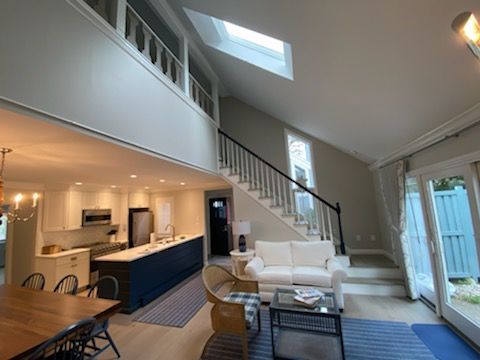 Bright open-plan living room and kitchen with white stairs, skylights, blue cabinets, and sliding glass doors.