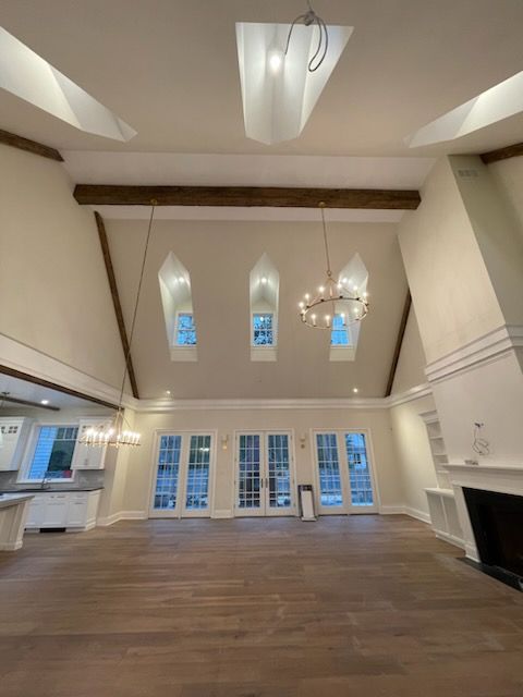 Spacious living room with vaulted ceiling, skylights, large windows, hardwood floors, and a chandelier.