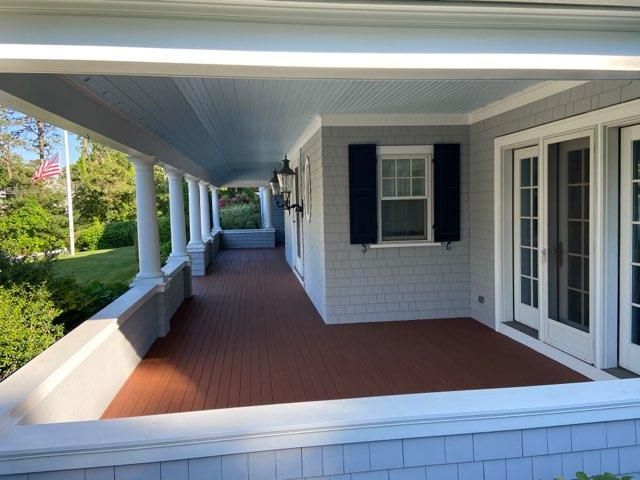Covered front porch with white columns, red floor, and white brick walls beside a lawn.