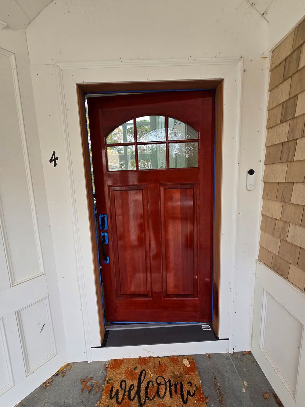 Red front door with arched window and a welcome mat on a porch