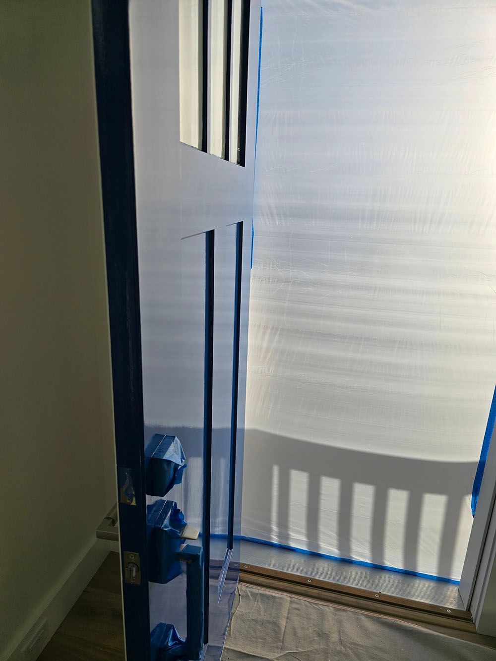 Open front door with blinds casting shadows on the floor inside a hallway