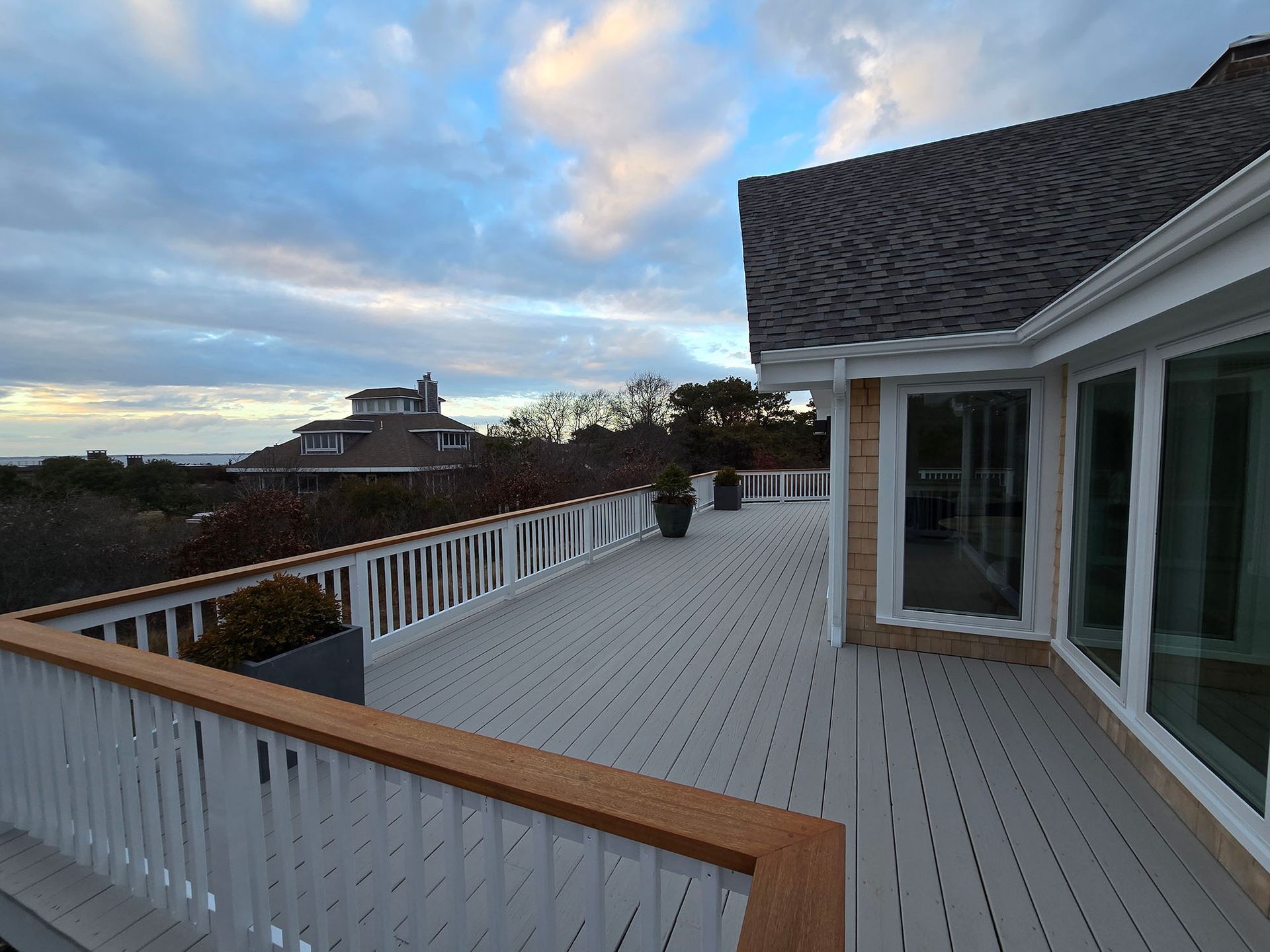 Spacious rooftop deck with white railing and wood trim overlooking a coastal sunset sky