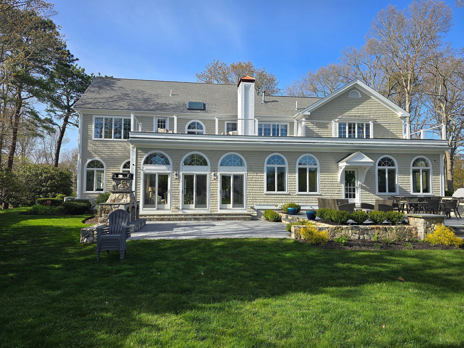 Large gray stone house with arched windows, white trim, and a green lawn under a clear blue sky
