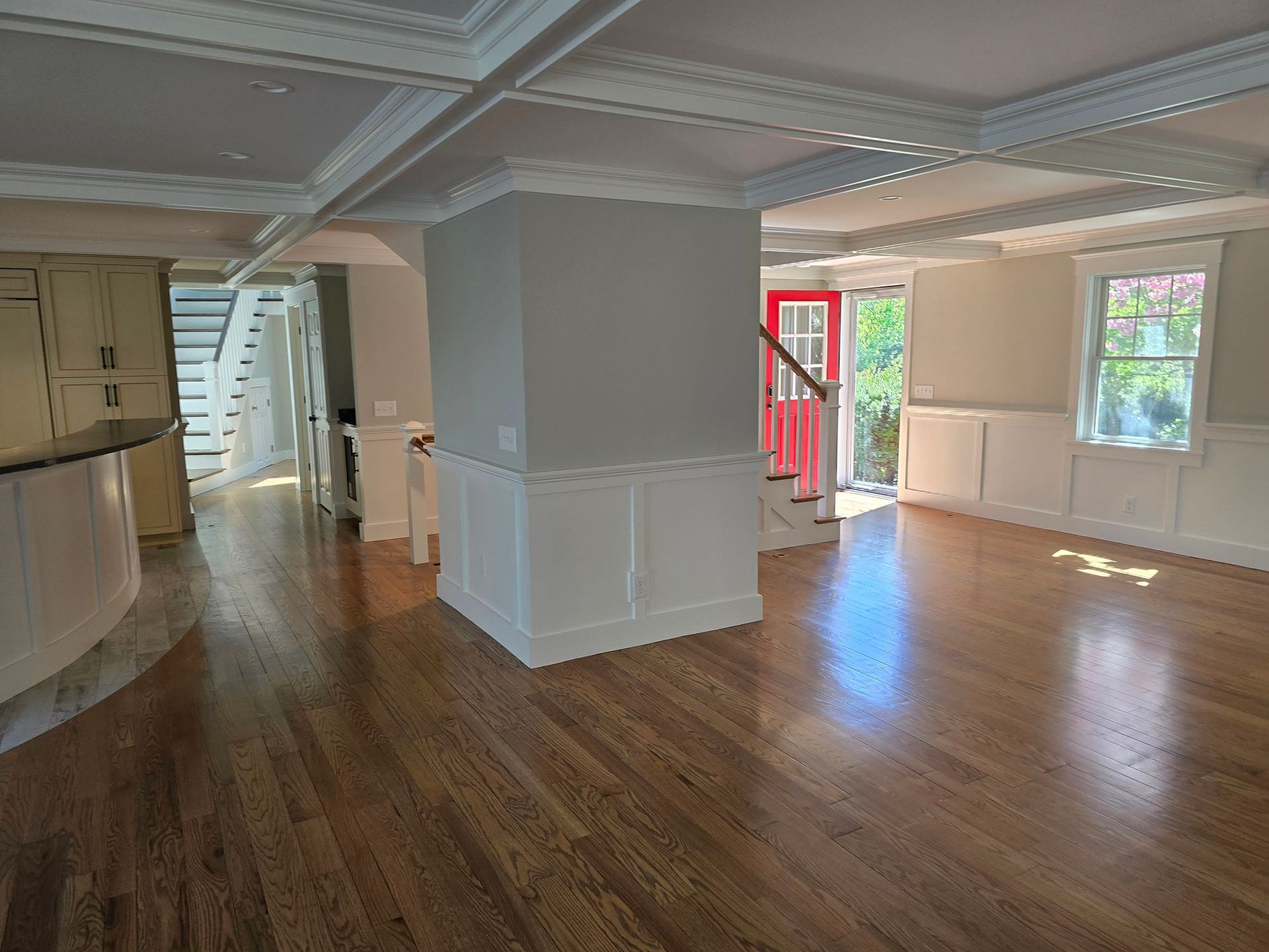 Empty hardwood-floored room with white trim, gray walls, and sunlight through windows and a glass door.