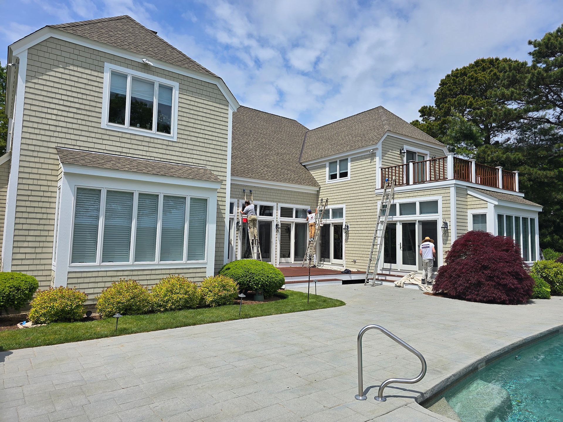 Large beige house with white trim and a poolside patio under a blue sky