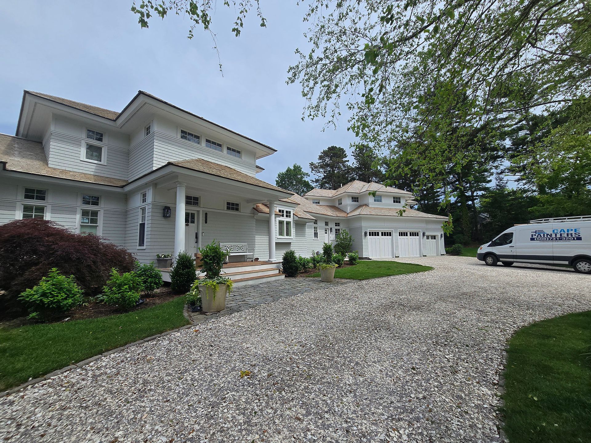 White two-story house with a gravel driveway, garage, and parked van on a sunny day