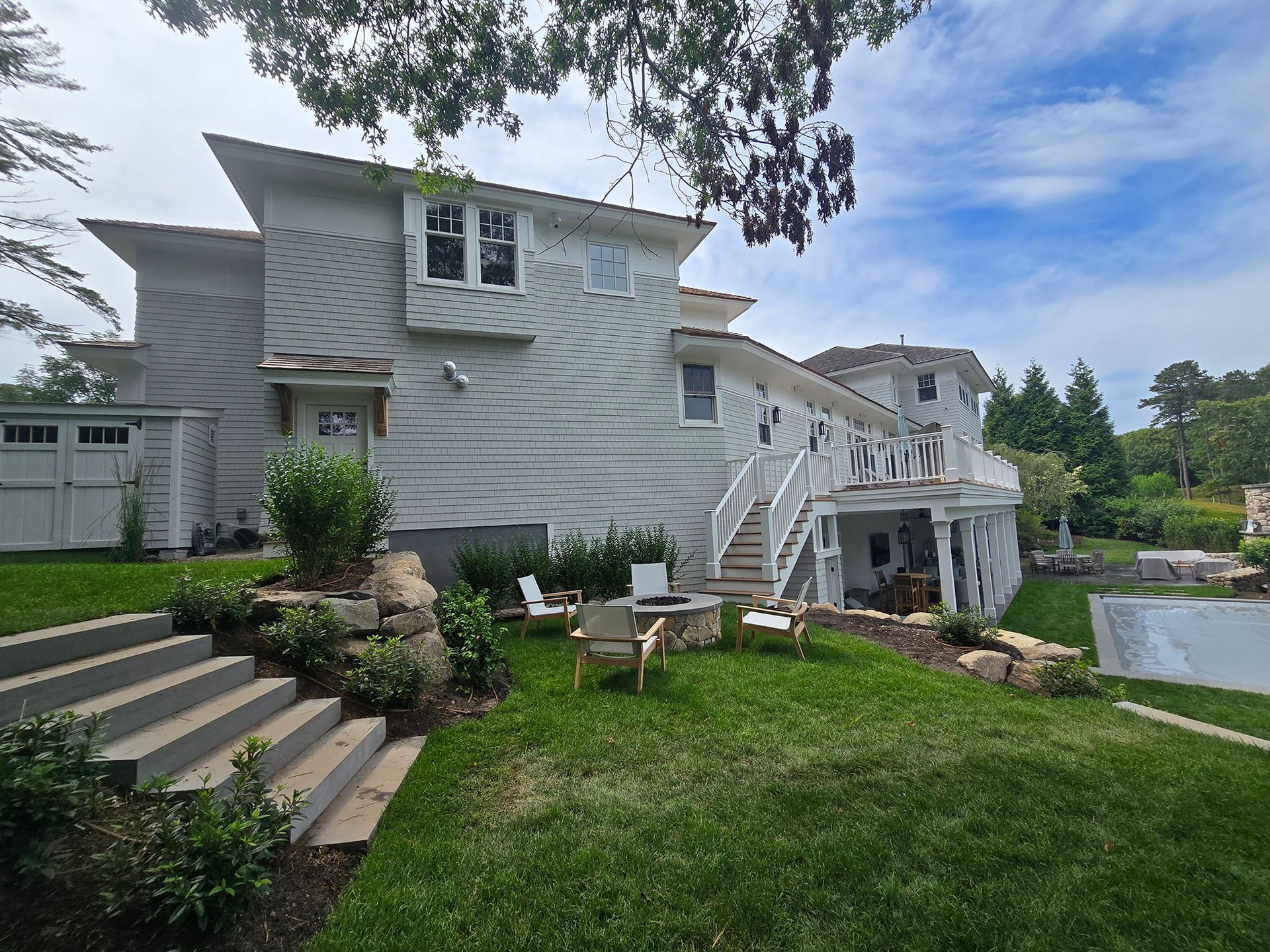White two-story house with deck, stairs, and a green lawn beside a pond