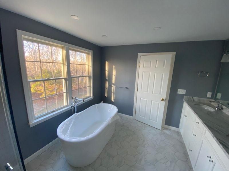 Modern bathroom with freestanding tub, large window, gray walls, white vanity, and tiled floor