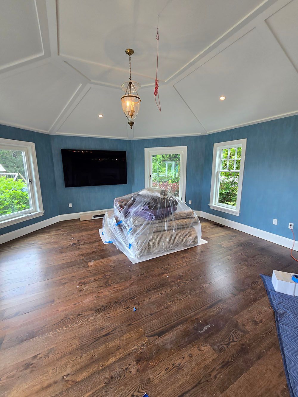 Blue living room with hardwood floors, white vaulted ceiling, fireplace, TV, and plastic-covered sofa.
