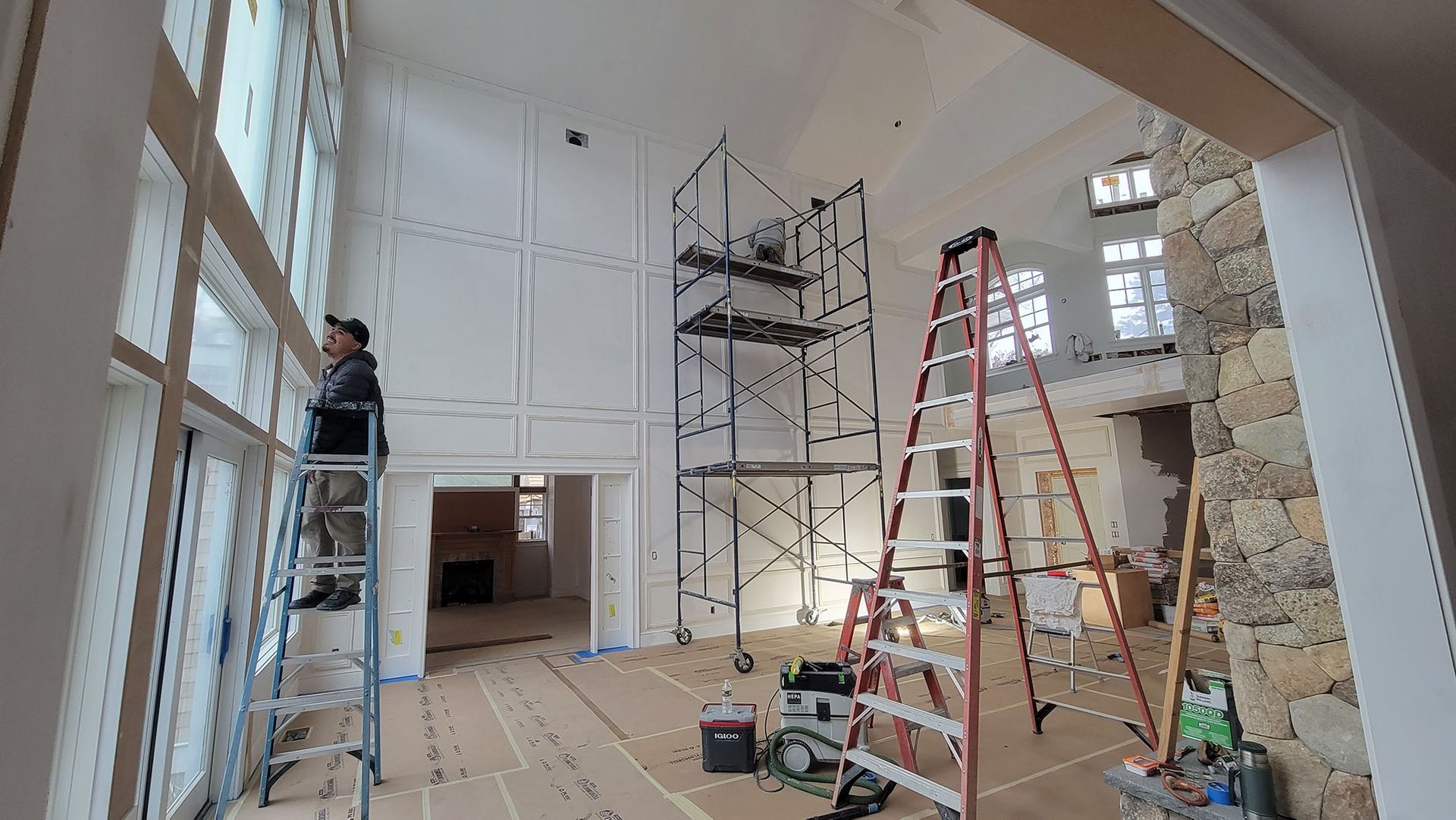 Renovation in progress inside a tall room with scaffolding, ladders, tools, and exposed walls.