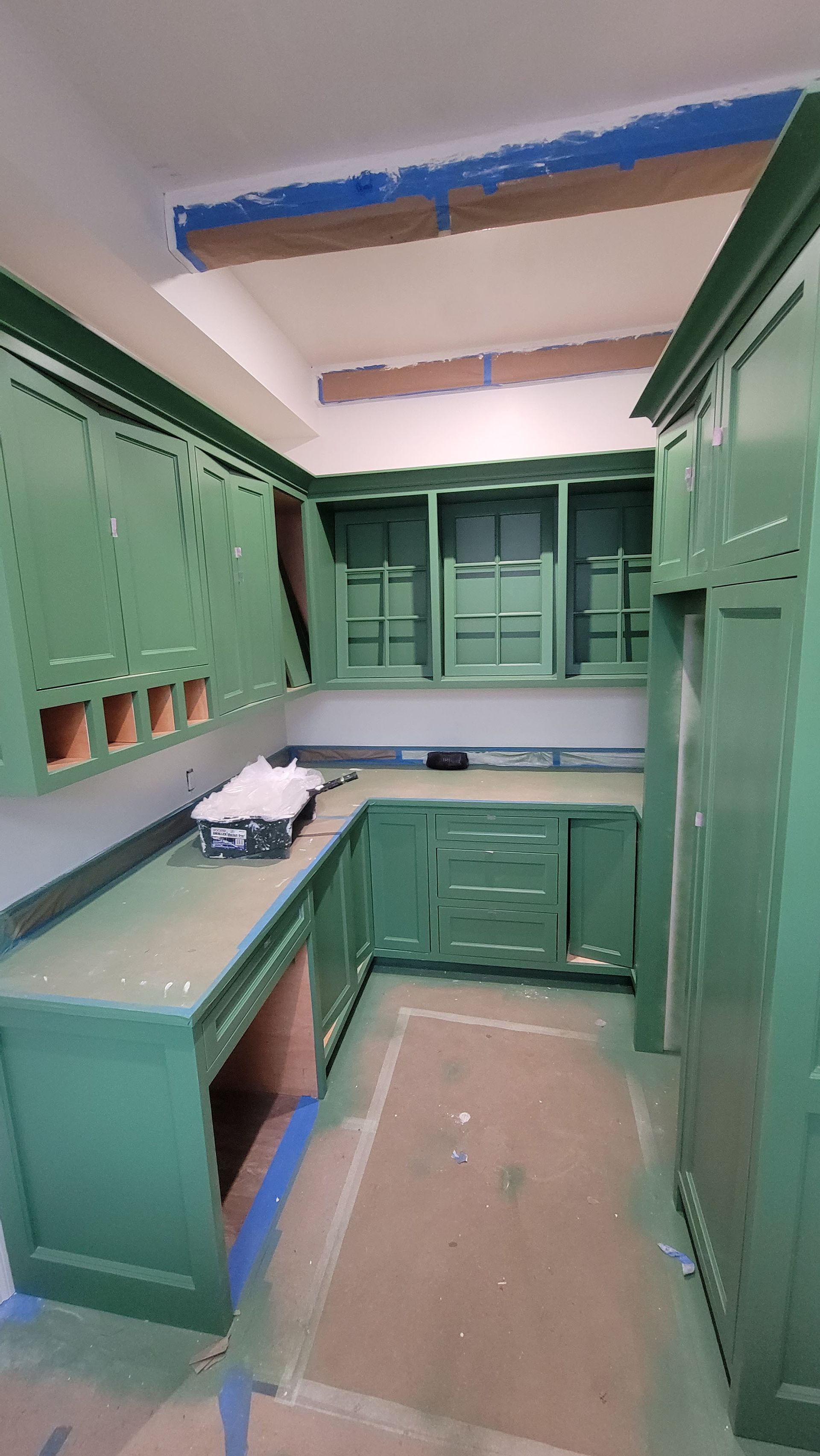 Green kitchen with cabinets on both sides, a countertop, and exposed ceiling beams under renovation