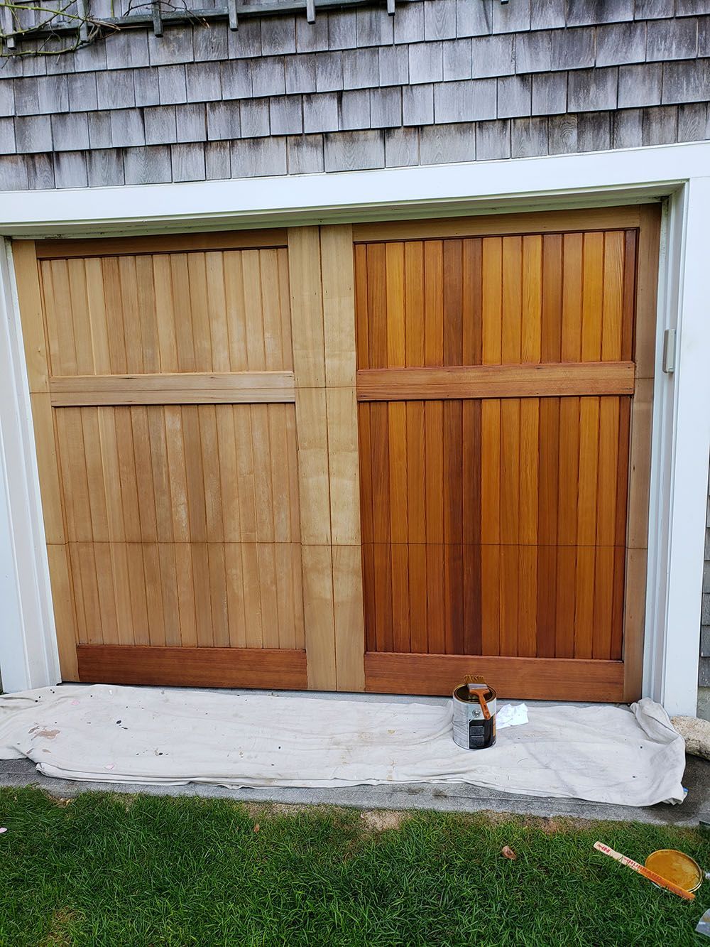 Closed wooden double doors on a house with a drink can on the step and grass in front