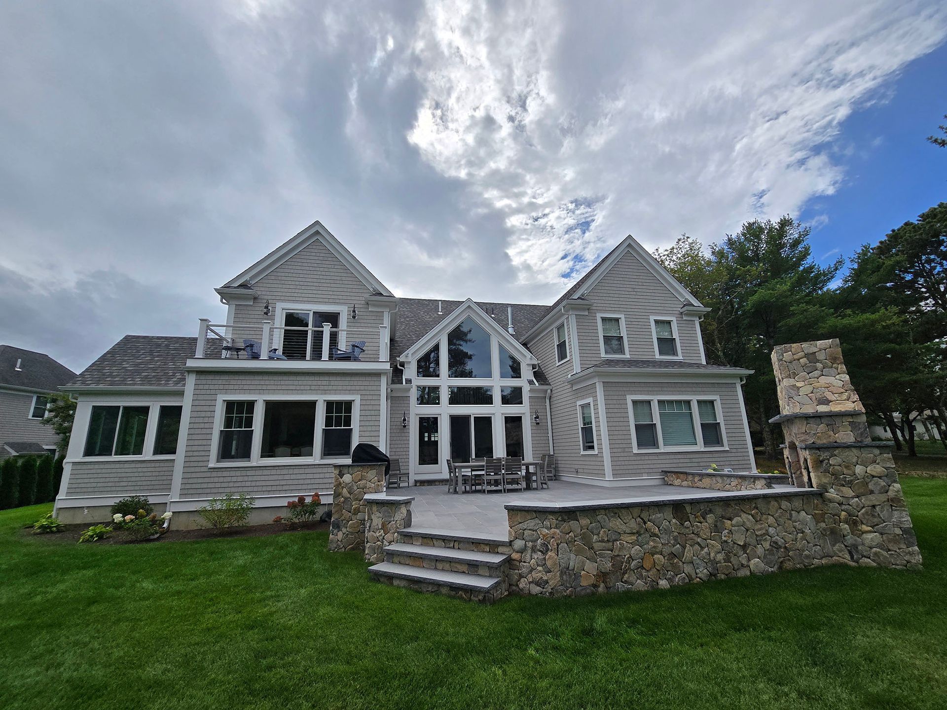 Large gray house with stone accents, front steps, and a manicured lawn under a cloudy sky