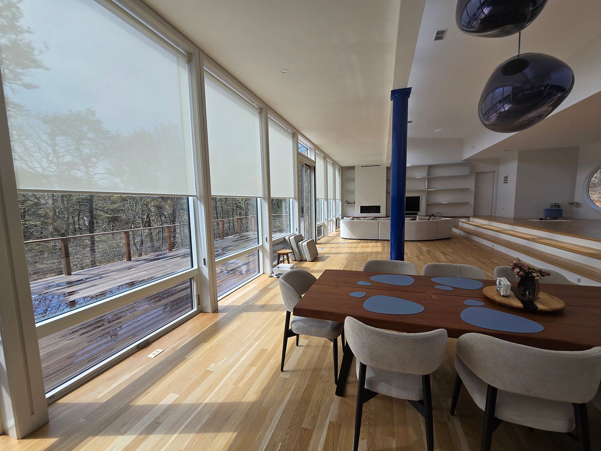 Bright modern dining room with large windows, wooden table, and white chairs overlooking snowy outdoors