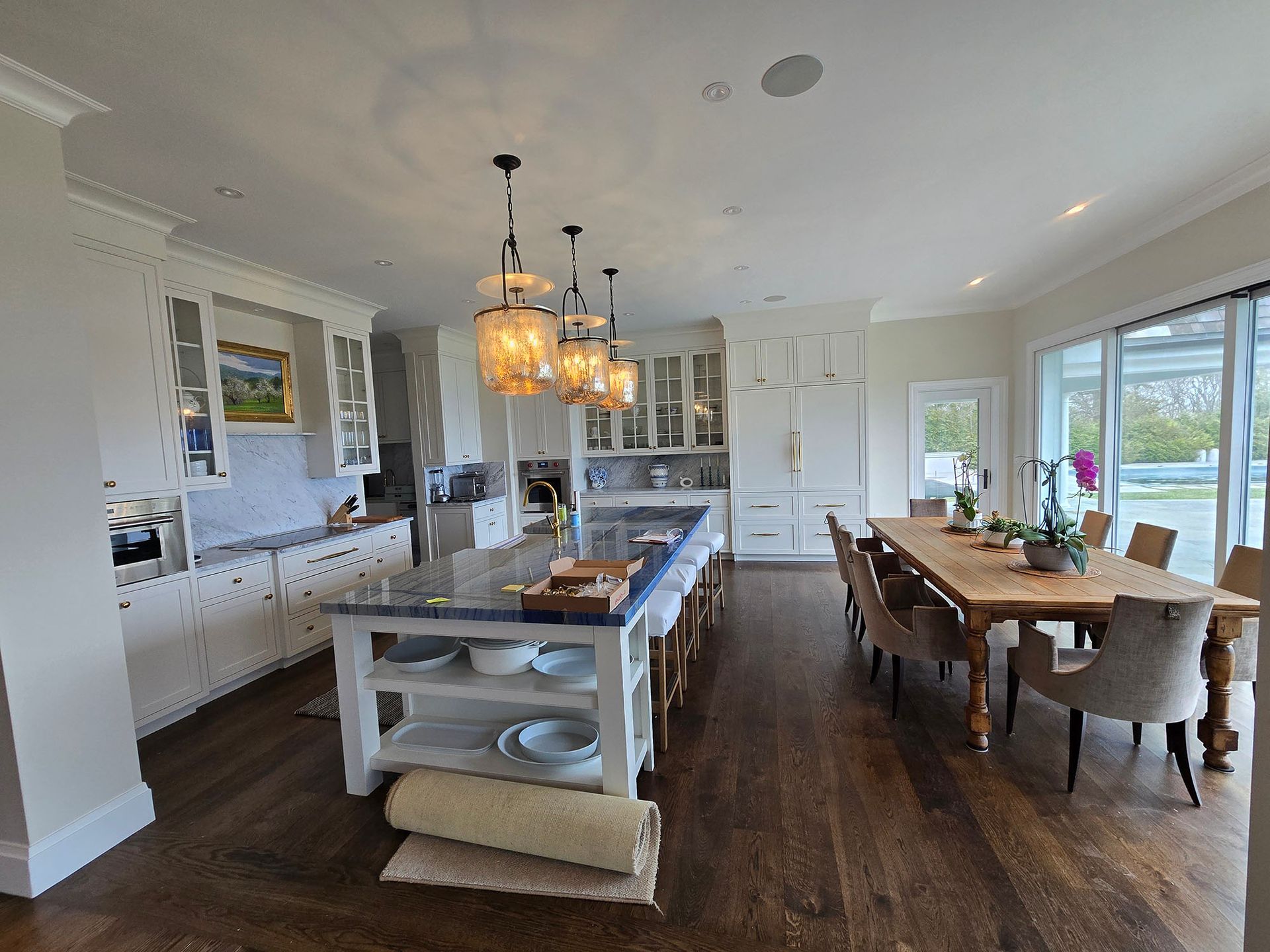 Bright open kitchen and dining area with island, dark wood floors, and large windows overlooking greenery