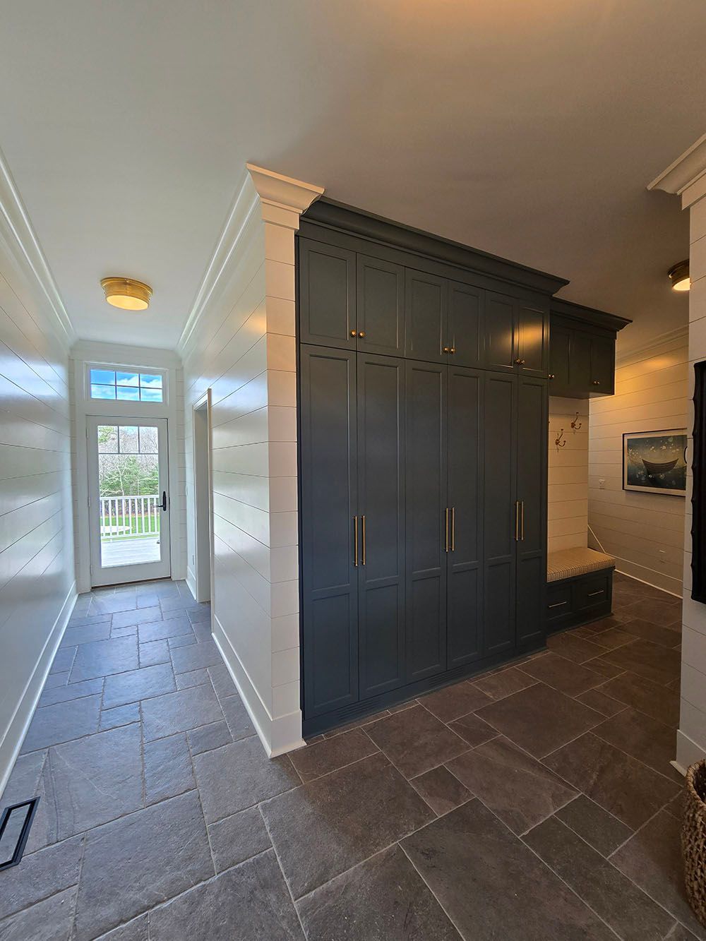 Hallway with dark gray built-in cabinets, tiled floor, and a doorway to a bright exterior on the left