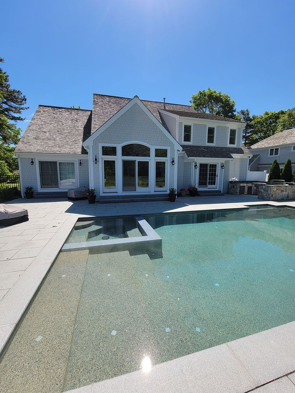 Modern house with a large backyard swimming pool and stone patio in bright sunlight