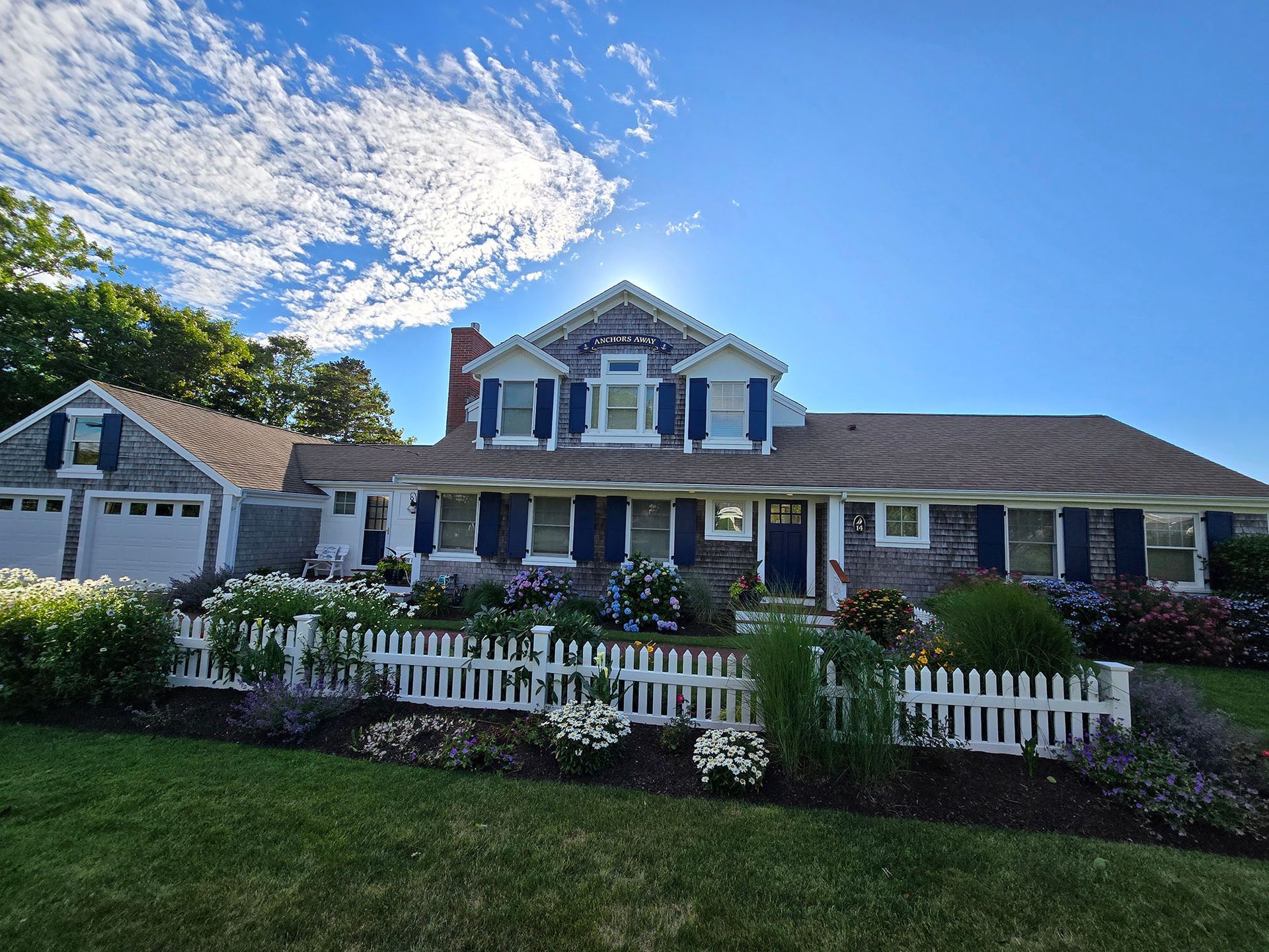 Suburban house with white picket fence, porch, and garage under a blue sky