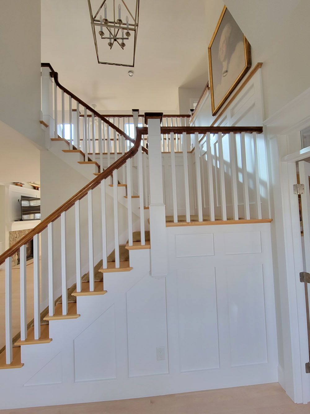 White staircase with wooden handrails and balusters in a bright hallway under a hanging light fixture