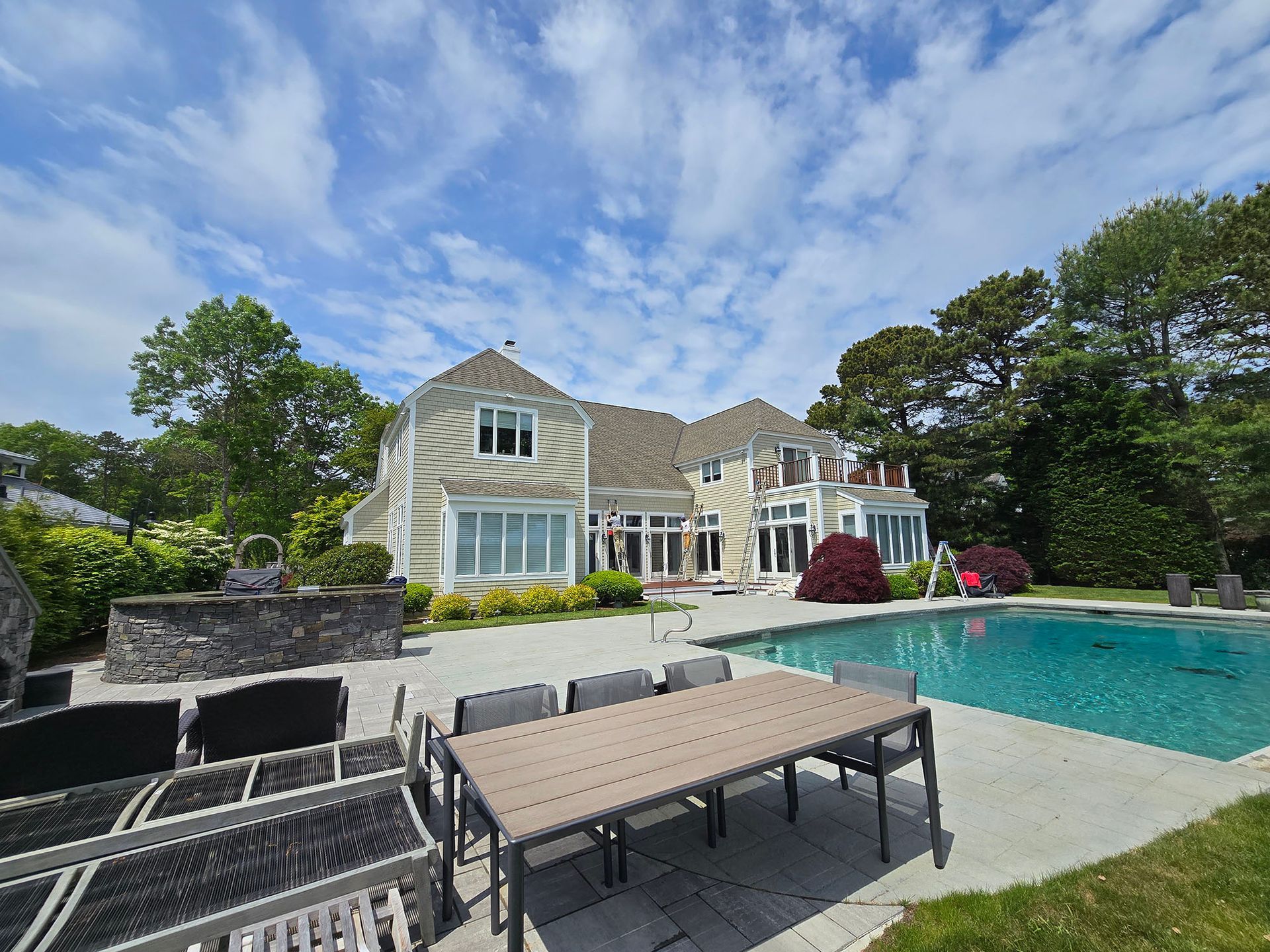 Backyard patio with pool, lounge chairs, and a large stone house under a blue sky