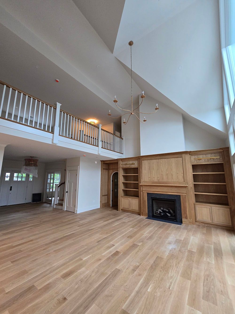 Bright open living room with vaulted ceiling, wood floors, built-in shelves, and a fireplace below a loft railing