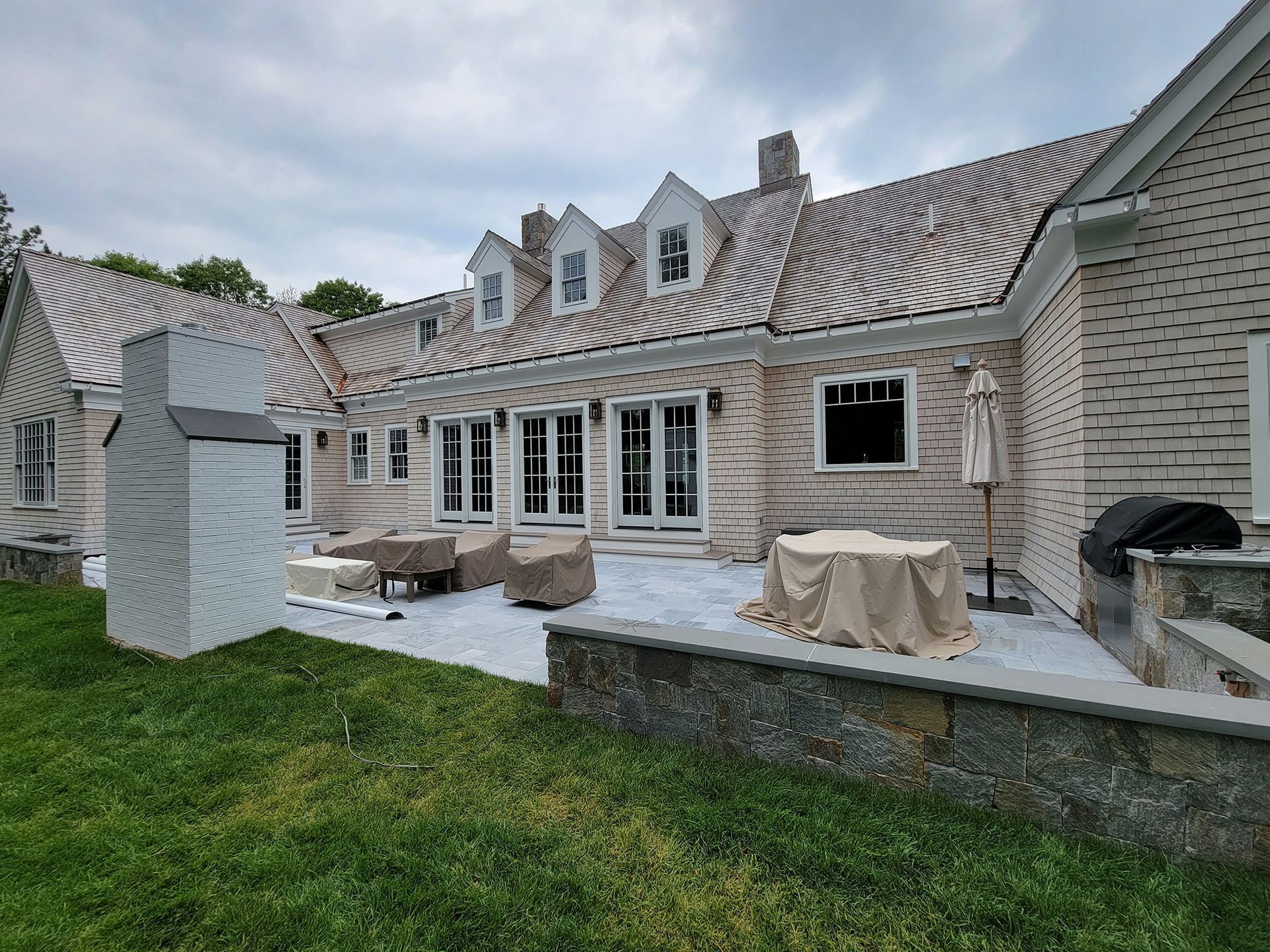Patio view of a stone house with striped awning, covered furniture, and a grassy backyard