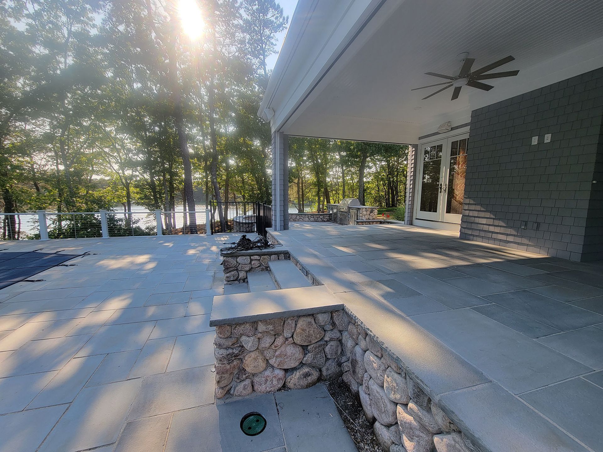 Covered patio with stone planter, outdoor tables, and wooded view in warm sunlight