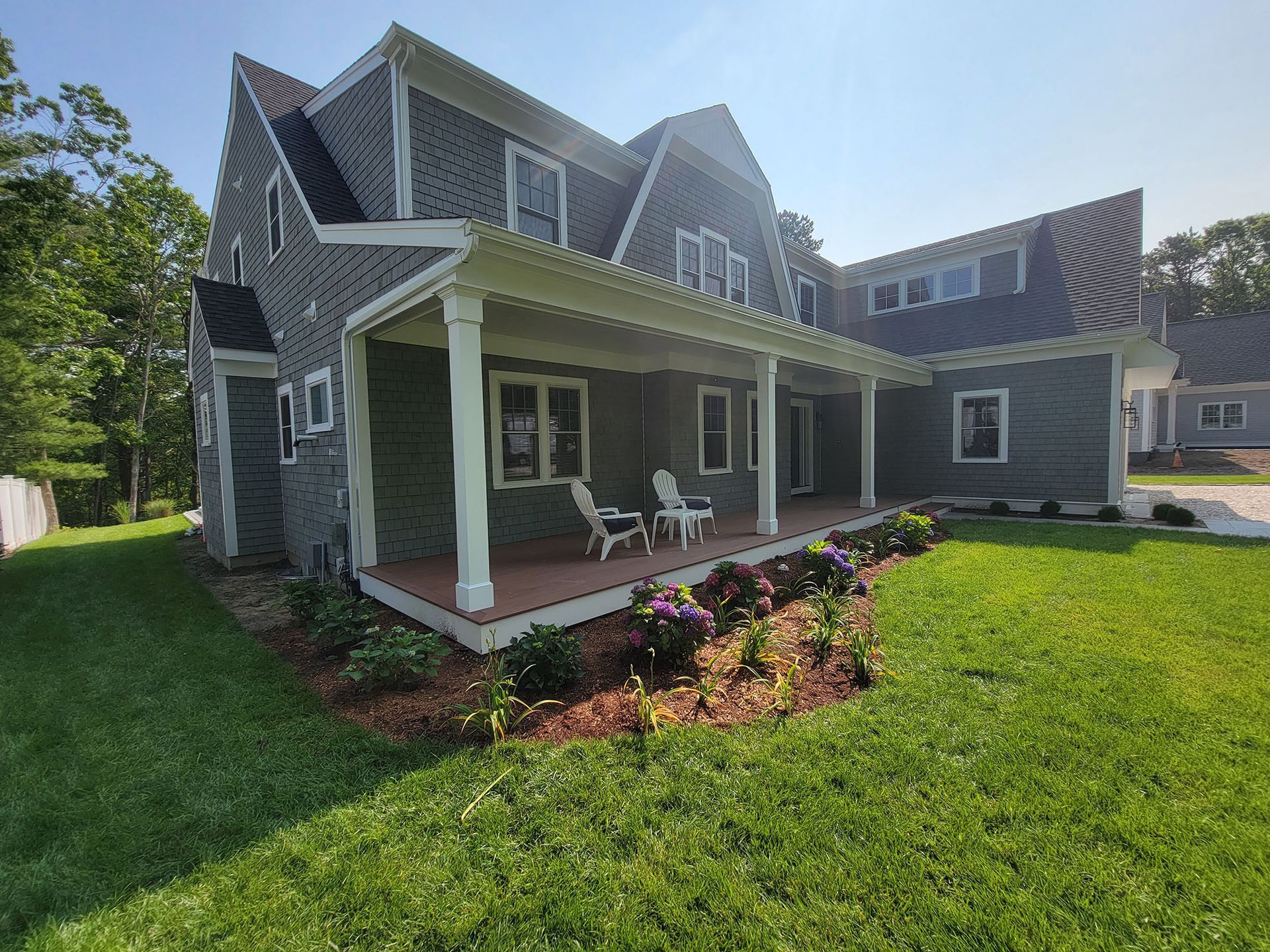 Gray house with white porch, two chairs, and a flower bed on a green lawn
