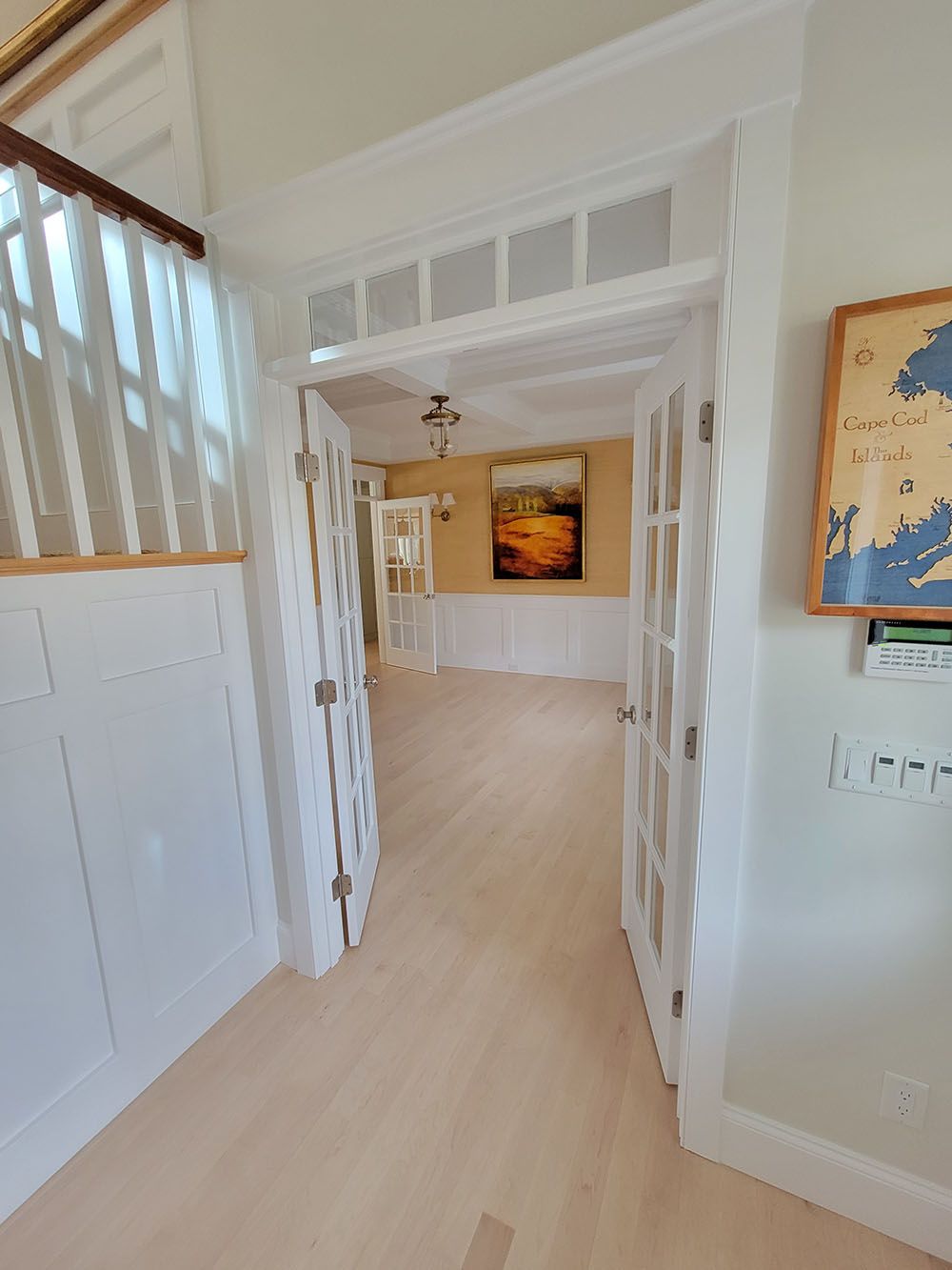 Bright hallway with white trim, open doors, and a painting on the far wall; light wood floors.