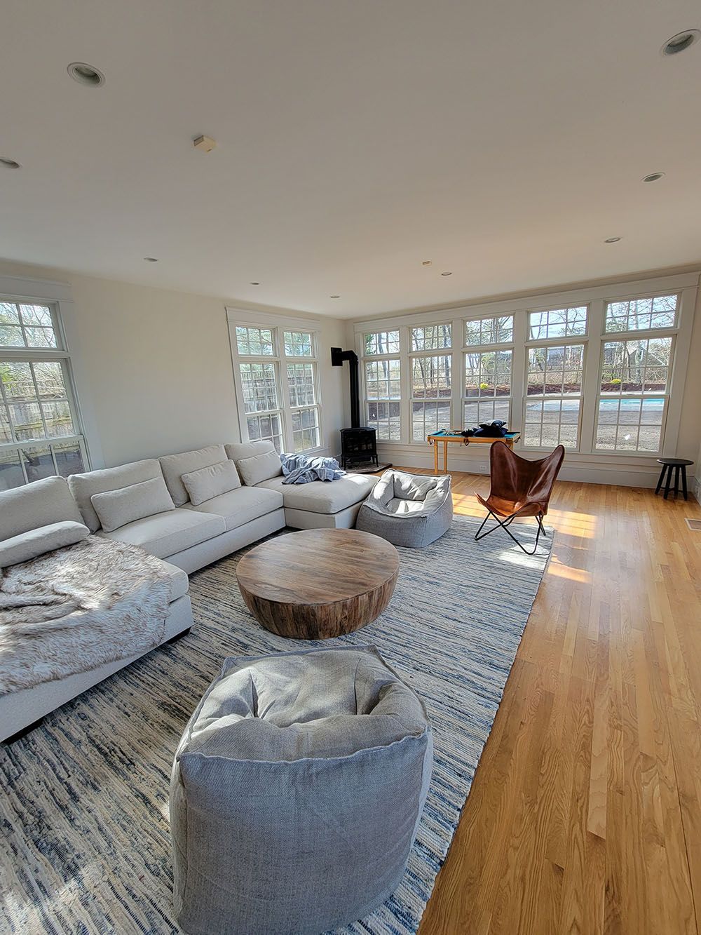 Bright living room with white sectional, gray ottoman, wooden coffee table, and large windows overlooking trees
