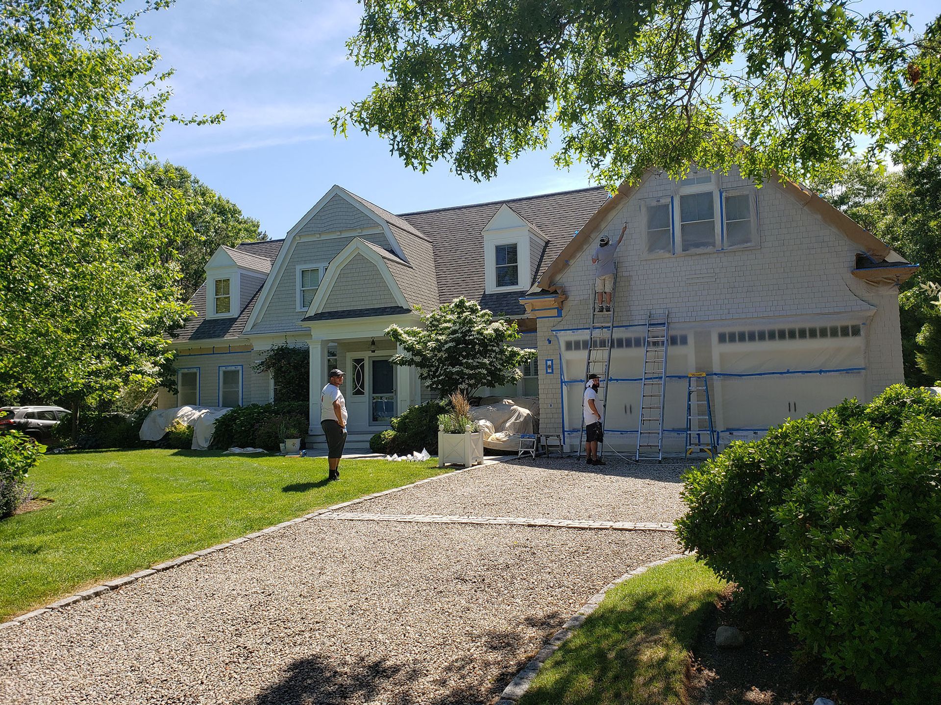 Two people standing outside a suburban house with a gravel driveway and green lawn