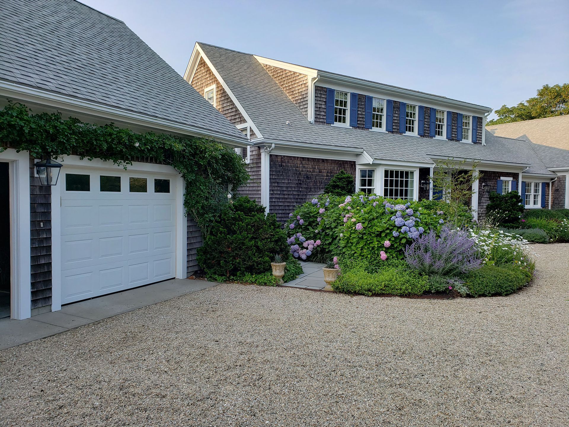 Suburban house with white garage, dormer windows, gravel driveway, and landscaped front garden