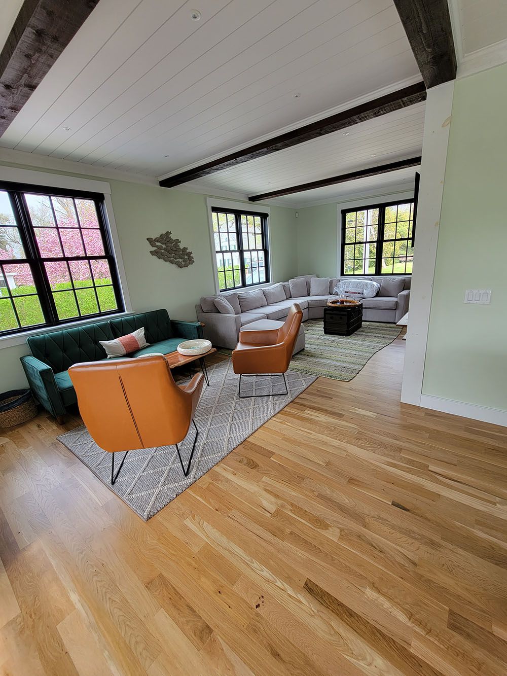 Modern living room with orange chairs, green sofa, gray sectional, and large windows
