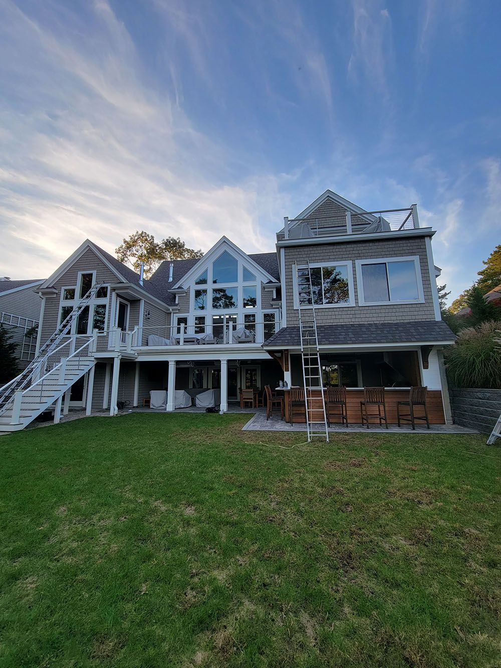 Large gray house with white trim and wraparound porch, seen from a grassy backyard at dusk