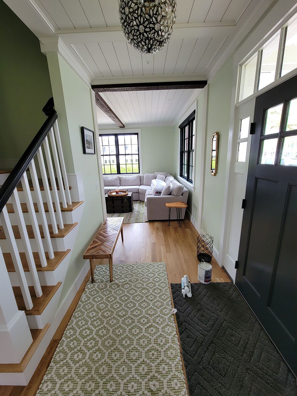 Bright entryway with staircase, patterned rug, bench, and a bedroom visible through an open doorway