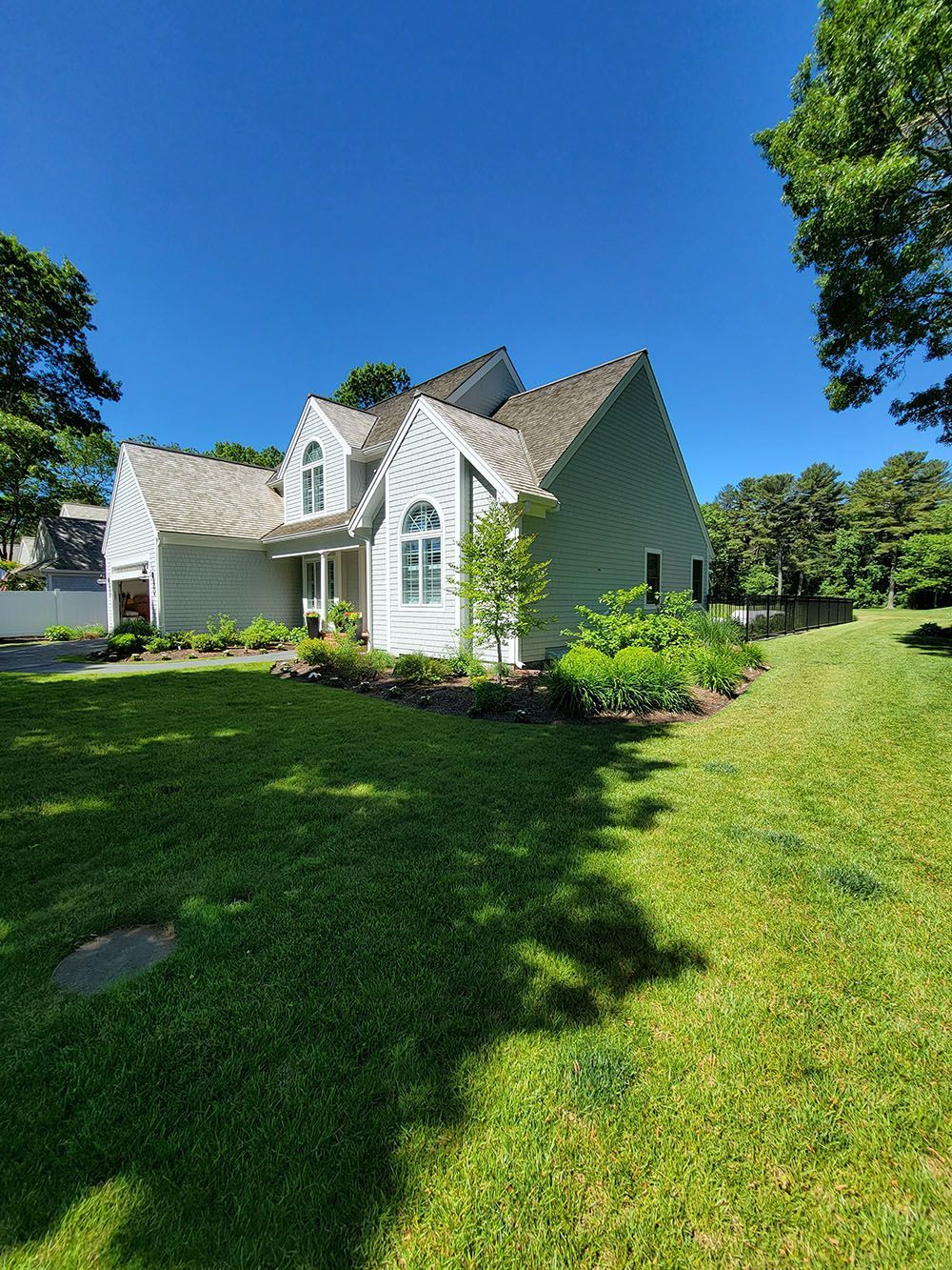 White house with steep roofs and large windows, surrounded by green lawn and trees under a clear blue sky