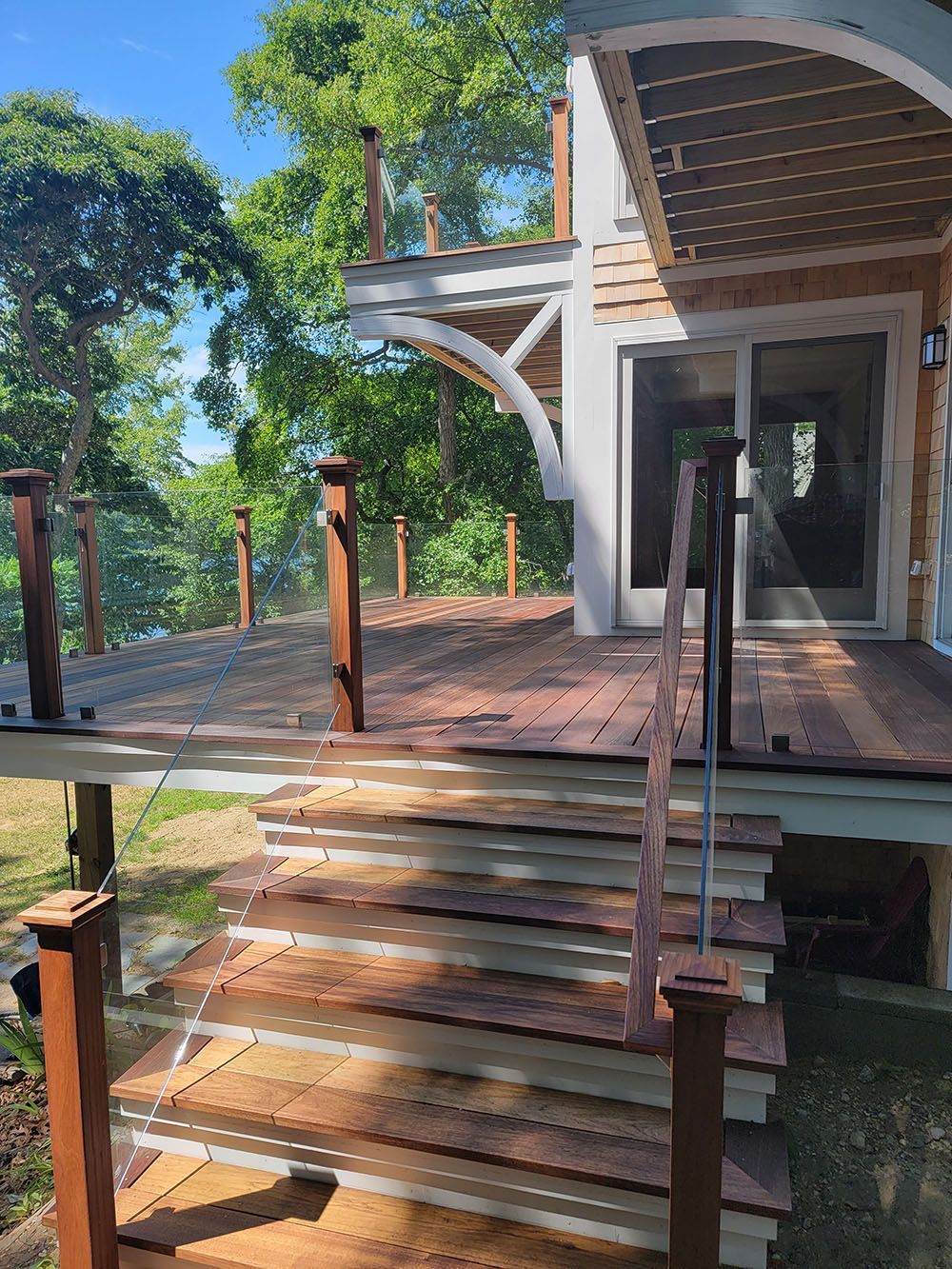 Wooden deck with stairs and metal railings leading to a house amid trees and greenery