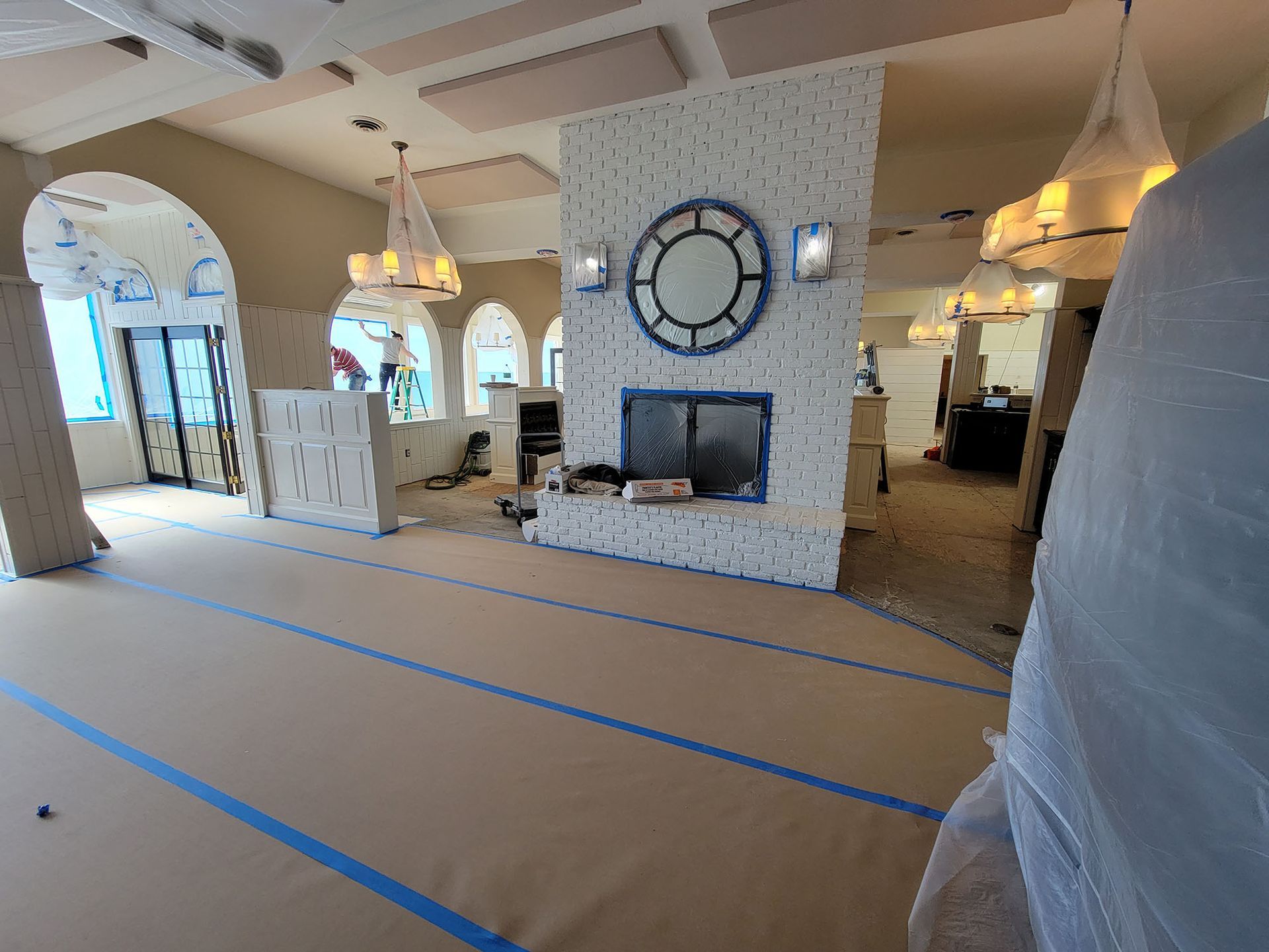 Unfinished open living room with taped-off floor, white fireplace, arched openings, and hanging lights