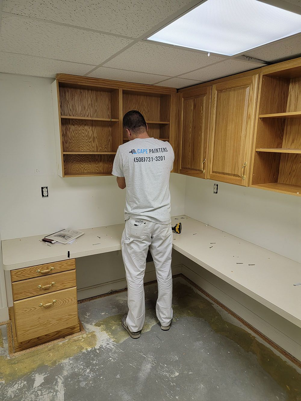 Person installing or repairing wooden cabinets in a small unfinished room, with debris on the floor.