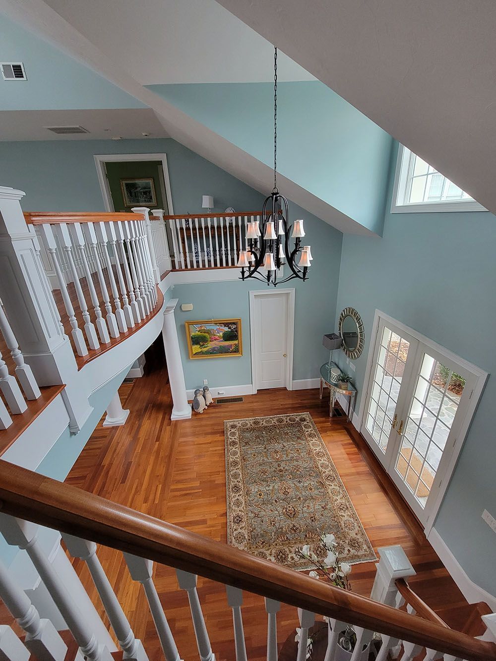 Bright two-story foyer with wood floors, blue walls, chandelier, staircase, and patterned rug